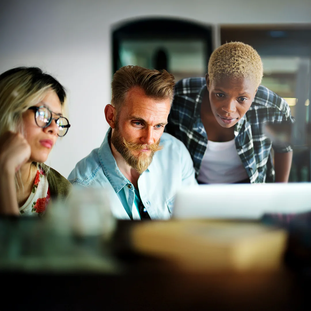 Three coworkers closely looking at a computer monitor together.