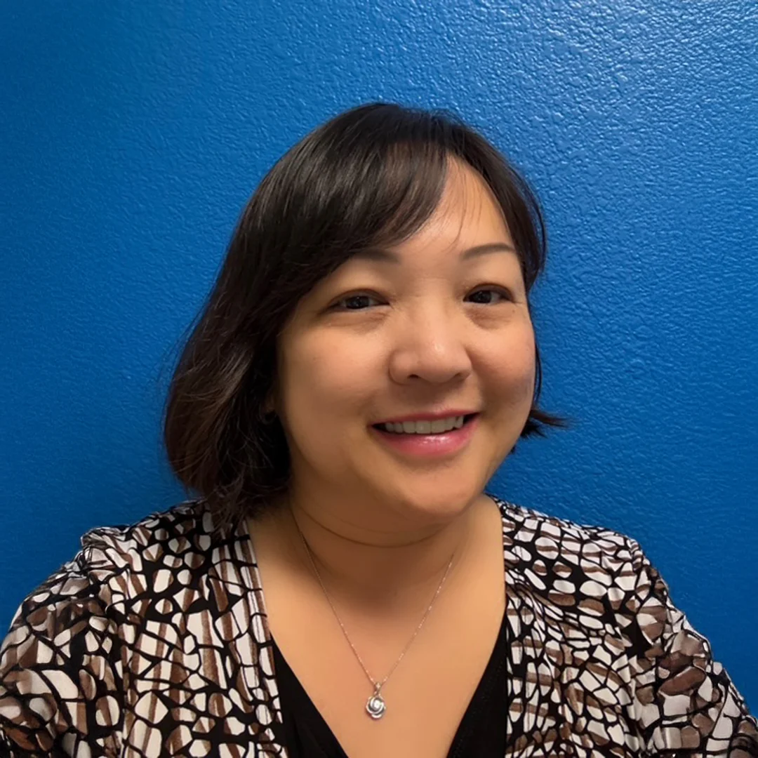 Anvi Dinh smiling in front of a bright blue wall, wearing a patterned blouse and necklace.