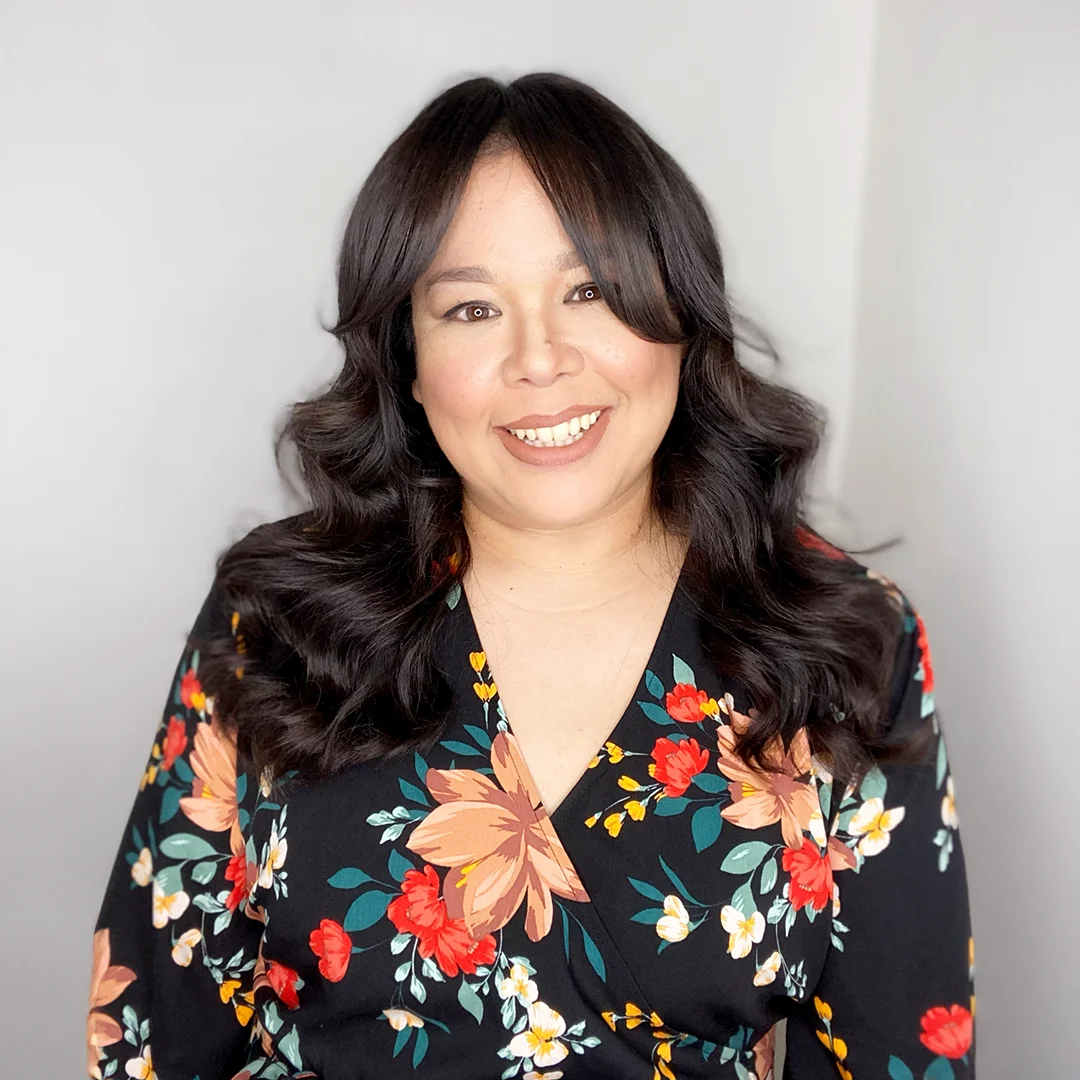 Lydia Marquez smiling in front of a light background, wearing a black floral dress.