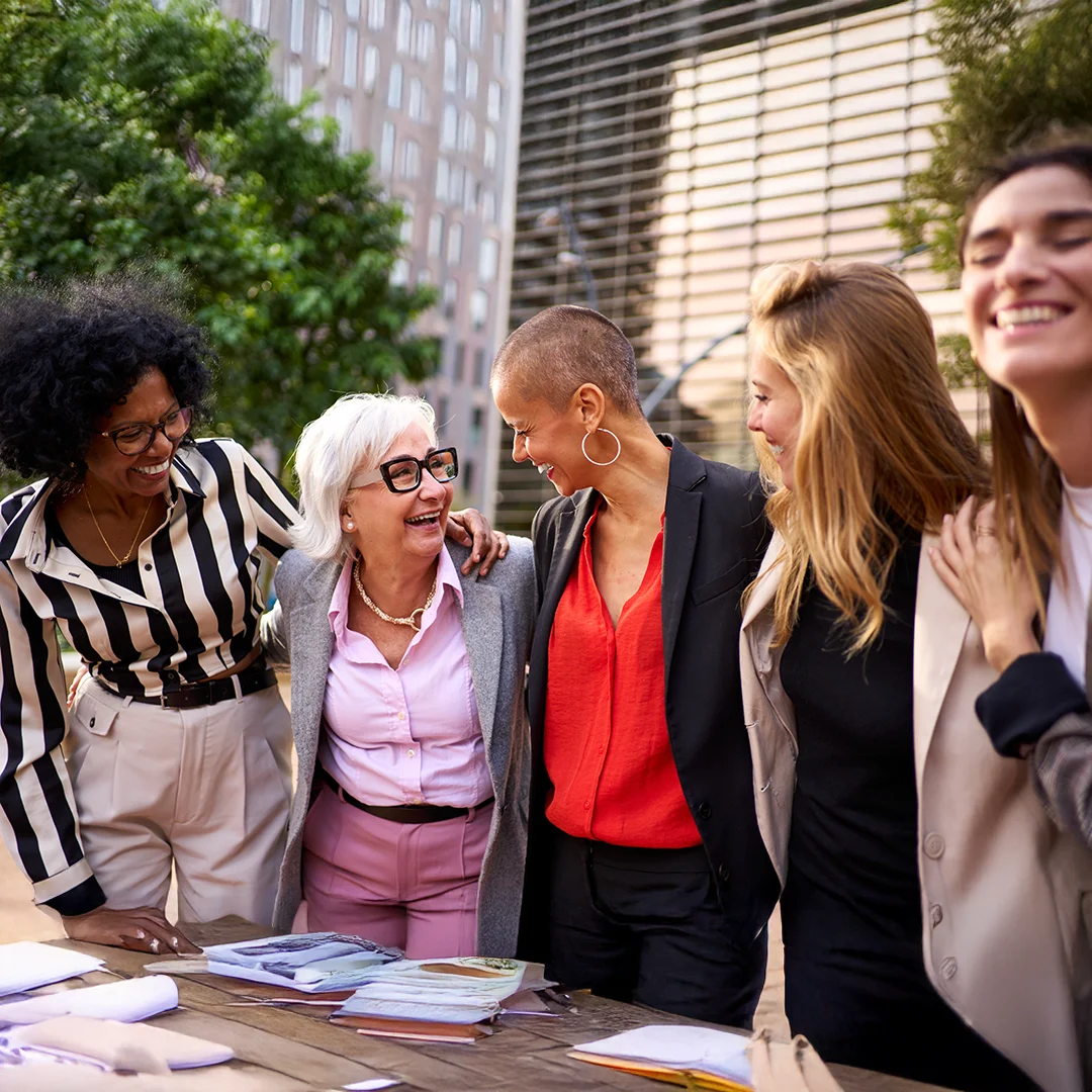 Group of women in business attire walking together and laughing outside a modern office building.
