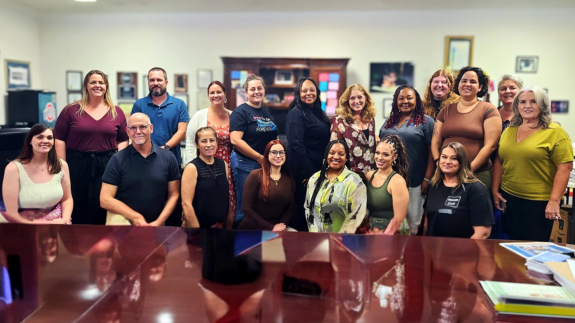 Group photo of SHIELD and CAPC team members smiling together indoors, posed in two rows.